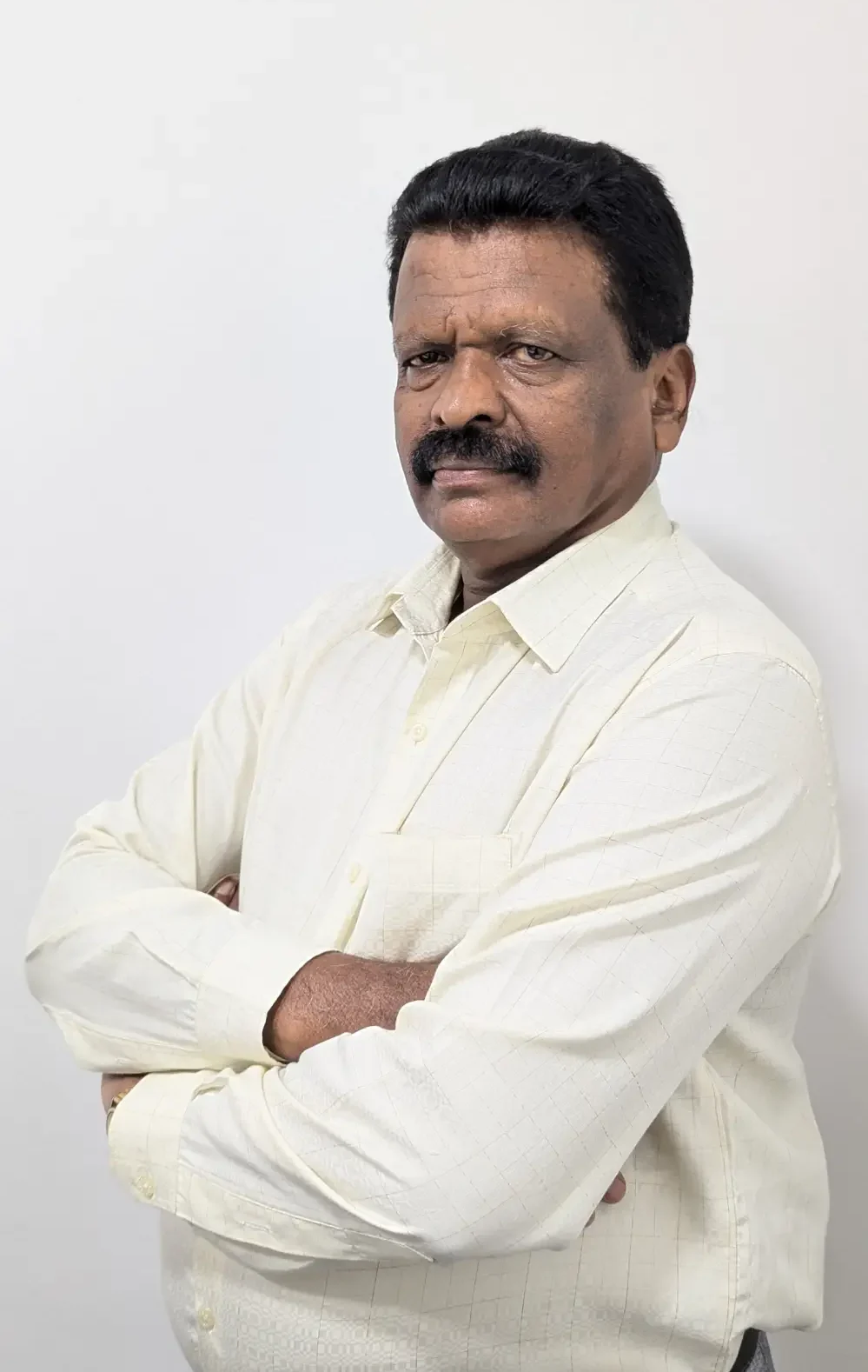 Man with a mustache, wearing a light-colored shirt, poses with arms crossed in front of a plain white background, depicting the professionalism inherent in Jane's integrated supply chain management.