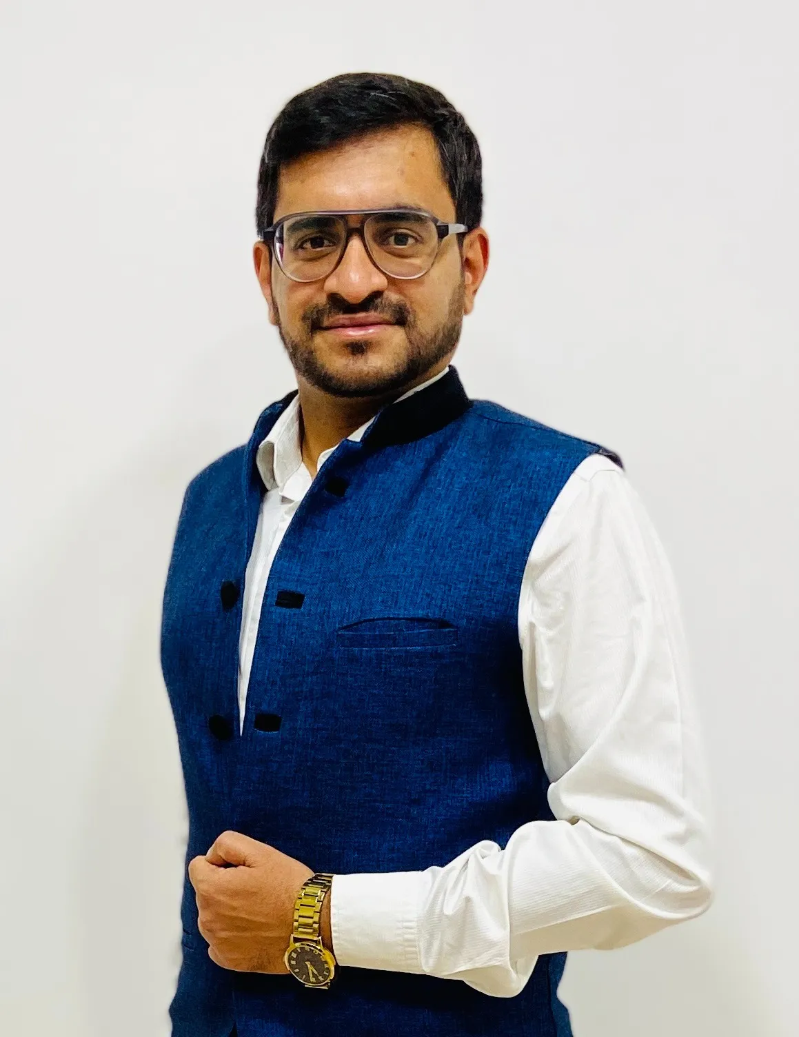 A man wearing glasses, a blue sleeveless vest over a white shirt, and a wristwatch stands against a plain white background, embodying the precision and efficiency of Jane's integrated supply chain management.