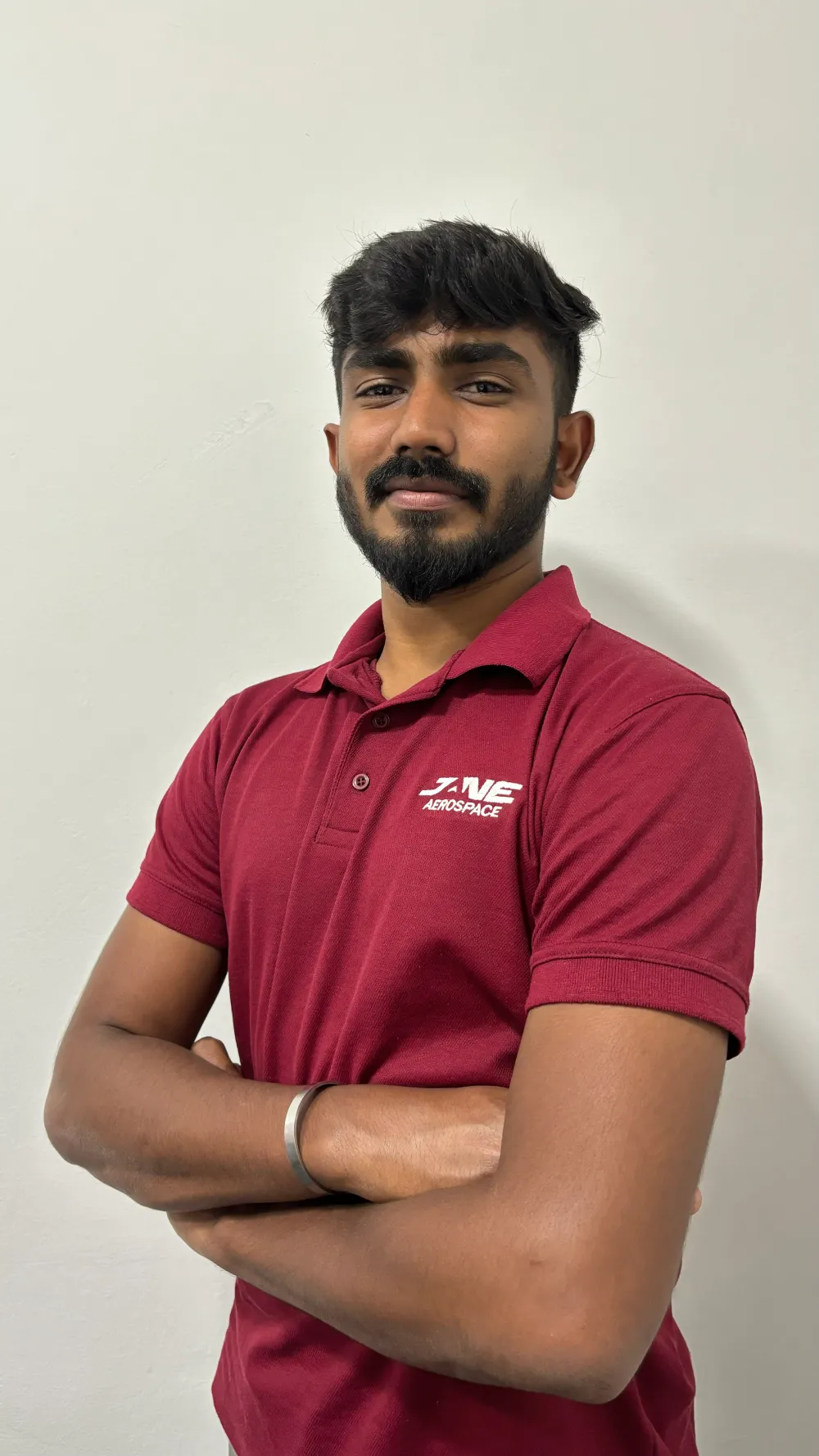 A man with a beard wearing a red polo shirt stands against a white background with his arms folded, confidently reflecting the expertise he brings to Jane's integrated supply chain management team.