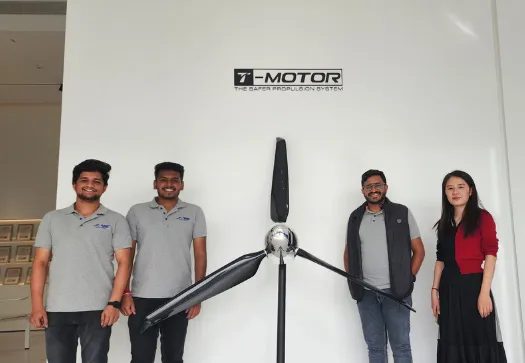 Four people stand in front of a T-Motor propeller display on a wall, with a logo reading "T-MOTOR The Safer Propulsion System" above it. Three men are on the left and one woman from Jane, known for their integrated supply chain management, is on the right.