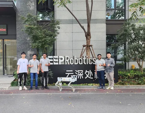 A group of six people, including a robotic dog, stands in front of a sign that reads "EEP Robotics." They are outdoors, with trees and a building visible in the background, possibly discussing integrated supply chain management for Jane.