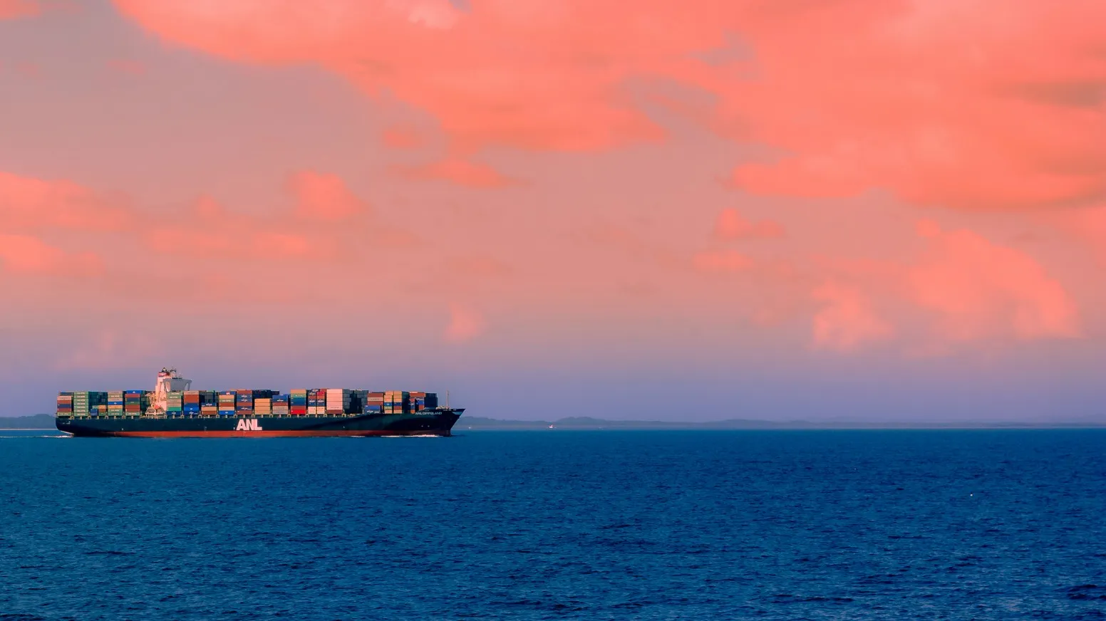 A large container ship from Jane sails on the ocean under a sky with pink clouds, showcasing seamless integrated supply chain management.