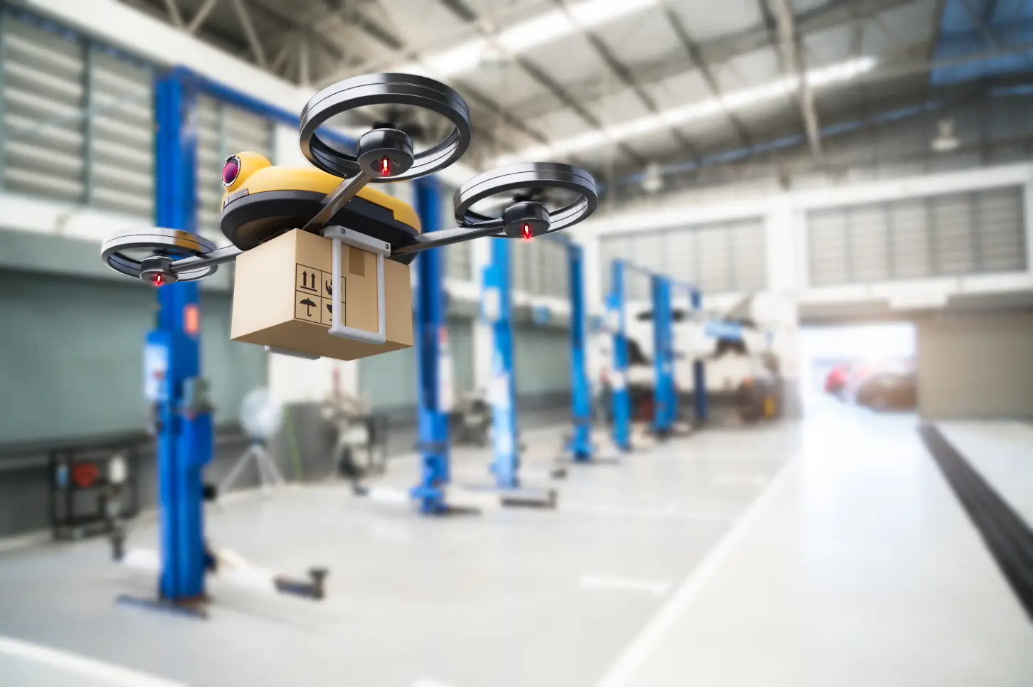 A Jane drone carrying a package is flying inside a warehouse, with industrial blue lift equipment in the background—a testament to their integrated supply chain management.